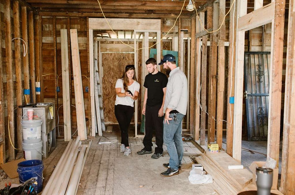 A woman showing her clients the progress of their remodel on her phone at a jobsite.  